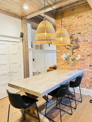 A long wooden dining table with black chairs, a rustic brick wall, and a rooster decoration. - The Modern Victorian Charmer Hot Tub 5 bedroom 4 bath (Atlanta)