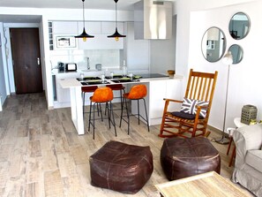 Eine moderne Küche mit weißen Schränken, ein Essbereich mit orangefarbenen Stühlen, ein Holzstuhl mit Sitzkissen und ein brauner Ledersitzhocker.