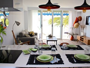 A dining area with a white table set for four, green plates, black placemats, and a view of the outdoors through large windows. - APARTAMENTO CABO AZUL by Interhome (El Campello/Villajoyosa)