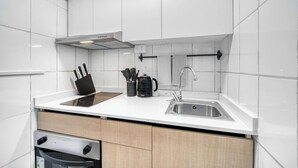 Ett modernt kök med vita kakelplattor, en diskho i rostfritt stål, en inbyggd ugn och en kaffebryggare.