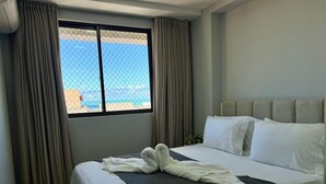 Une chambre d’hôtel avec un lit, des rideaux, une fenêtre donnant sur un paysage agréable et une tête de lit.