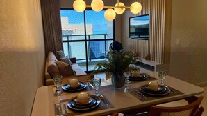 Un coin repas avec une table dressée pour quatre personnes, un canapé en arrière-plan et une grande fenêtre donnant sur un beau paysage.