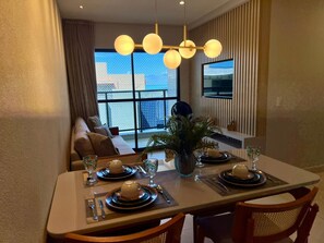Ein Essbereich mit einem Tisch für vier Personen, einer Couch im Hintergrund und einem großen Fenster mit Blick.