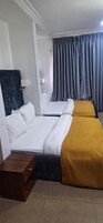 Habitación de hotel con dos camas, una mesita de noche de madera, cabecera y un ventanal grande con cortinas.