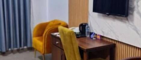 A room with a dining table, two yellow chairs, a television mounted on the wall, and a wooden panel design.