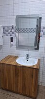 Un baño con tocador de madera, lavamanos blanco y espejo.