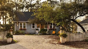 Une maison avec une allée en gravier, une clôture blanche en bois et une véranda ornée de plantes en pot.
