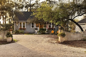 A house with a gravel driveway, a white picket fence, and a porch with potted plants. - Lovely 2-bedroom waterfront cottage with many outdoor activities and charm (Foley)
