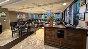 Una àrea de menjador àmplia, amb diverses taules i cadires, una zona de bar central i un sostre amb il·luminació empotrada.