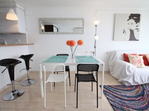 A modern living room with a white sofa, a colorful rug, a dining table with chairs, and a kitchen area with a hanging light. - LOFT PLAYA MUCHAVISTA by Interhome (El Campello/Villajoyosa)