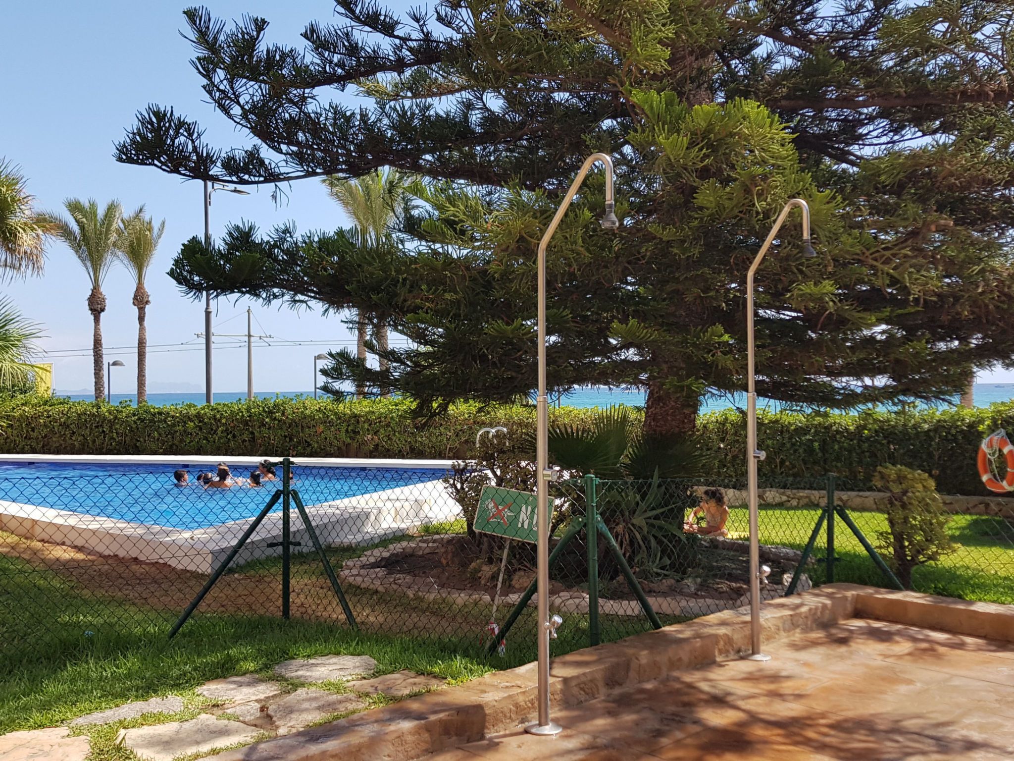 Une piscine entourée d’une clôture, équipée d’une bouée de sauvetage et d’un panneau affichant un symbole de croix rouge.