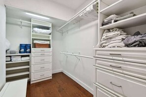 Ein begehbarer Kleiderschrank mit weißen Regalen, Schubladen und Ablageflächen, der ordentlich gefaltete Kleidung und Aufbewahrungsboxen zeigt.