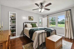 A bedroom with a bed, a bedside table, a ceiling fan, a window with curtains, and a built-in shelf with decorative items. - Spacious 4BR + 3.5BA Home, Backyard, Tampa & USF (Lutz)