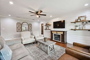 A living room with a fireplace, a ceiling fan, and a mounted TV. - Spacious 4BR + 3.5BA Home, Backyard, Tampa & USF (Lutz)