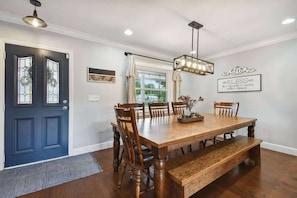 A dining room with a wooden table, six chairs, a bench, a chandelier, and a blue door with glass panels. - Spacious 4BR + 3.5BA Home, Backyard, Tampa & USF (Lutz)