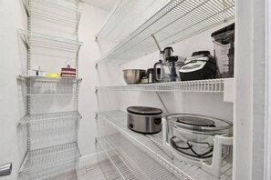 Een keuken met metalen planken en diverse apparaten, waaronder een koffiezetapparaat en een slowcooker.