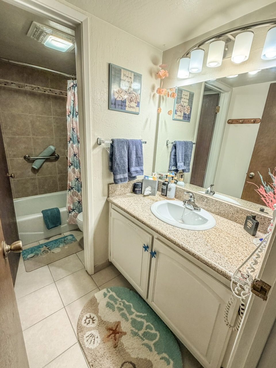 A bathroom with a sink, mirror, towel rack, shower curtain, and a decorative rug.