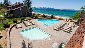 Área da piscina com duas piscinas, espreguiçadeiras e vista para a praia e montanhas.