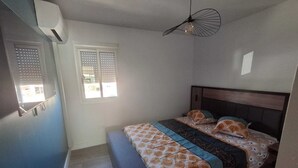 Een slaapkamer met een bed, een bankje, een plafondventilator en een raam met jaloezieën.