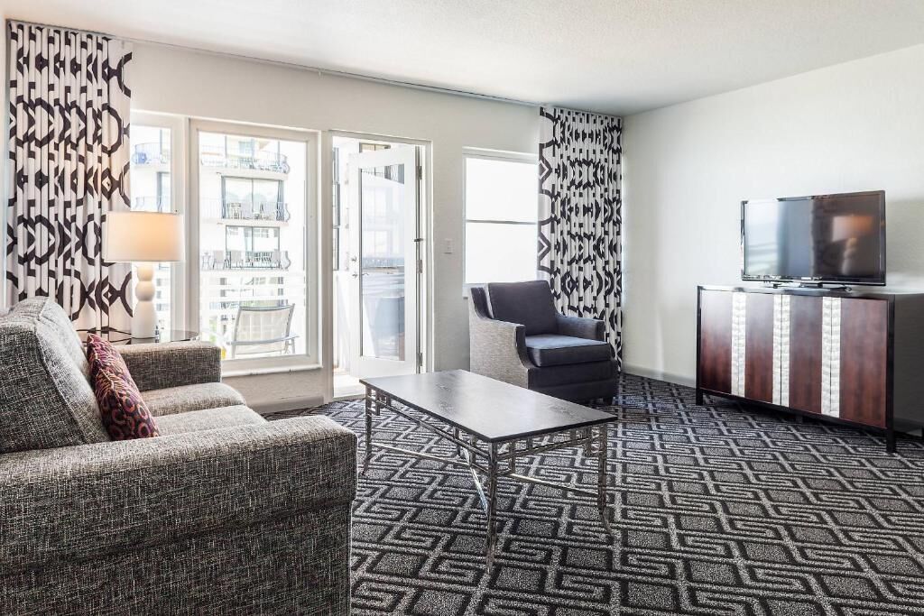Habitación de hotel con sofá, sillón, televisión y alfombra estampada.