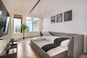 A modern living room with a grey sofa, a flat-screen TV, and three framed artworks on the wall.