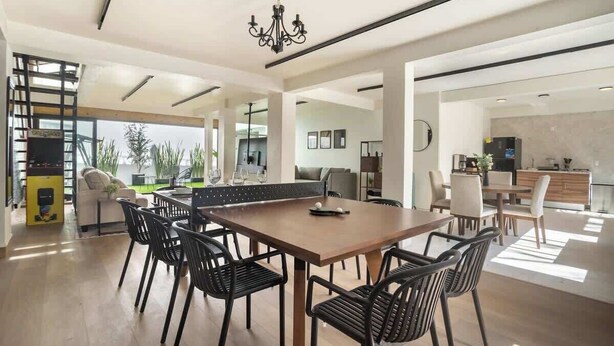 A spacious dining area with a wooden table and black chairs, a chandelier, and a view of the outdoors. - Spacious Home Ideal for Groups, Patio, Arcade Game (Mexico City)
