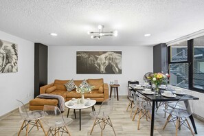 Ein modernes Wohnzimmer mit einer Couch, klaren Stühlen, einem Esstisch und Kunstwerken an den Wänden.
