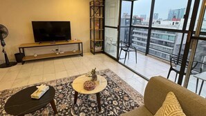 Ein modernes Wohnzimmer mit einer Couch, einem Couchtisch, einem Fernseher und einem Balkon mit Blick auf die Stadt.