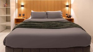 Ein modernes Bett mit Holz-Kopfteil, ein Nachttisch mit Lampe und ein Regal mit Dekoration.