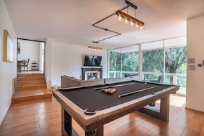 A pool table in a room with a large window, a television, and a staircase leading to another area. - Spacious Home for Groups with Garden & Game Room (Naucalpan de Juárez)