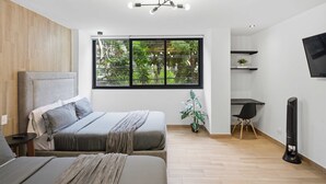Quarto moderno com cama, mesa de cabeceira e uma janela grande com vista para o verde.