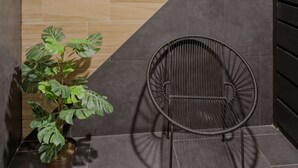 Um canto com parede revestida de azulejos escuros, uma parede de destaque em madeira, uma planta em vaso e uma cadeira preta de arame.