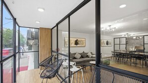 Um interior moderno com paredes de vidro, chão de madeira, um sofá, uma mesa de jantar e cadeiras.