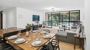 Uma zona de refeições moderna com uma mesa de madeira posta para seis pessoas, rodeada por cadeiras pretas.