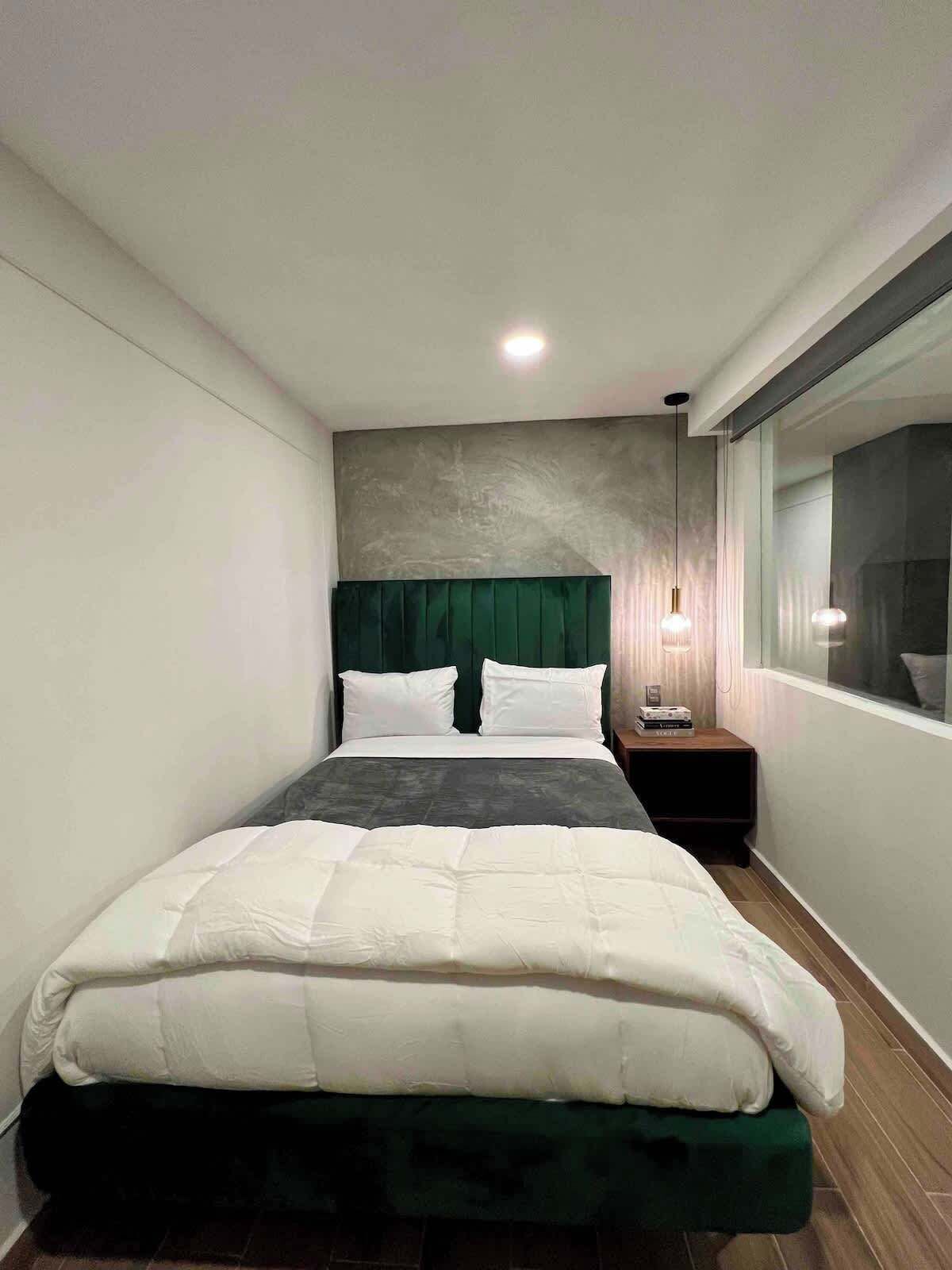 A modern bedroom with a bed, a nightstand, a window, and a wall-mounted light fixture.
