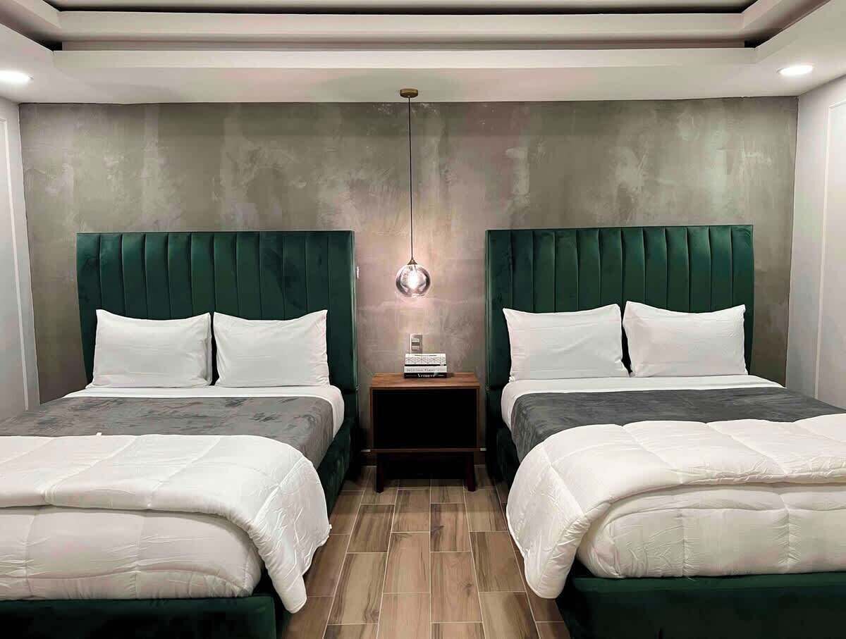 A double room with two beds, a nightstand, a wall-mounted light, and a ceiling light.