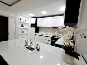 A modern kitchen with white cabinetry, a marble countertop, and a vase of white orchids. - Espace Virage type F4 (Dakar)