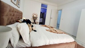 Ein Schlafzimmer mit einer gepolsterten Kopfteile, einem Bett mit weißer Bettwäsche, einem Nachttisch mit Lampe und einer Wanddekoration.