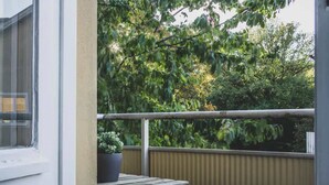 Ein Balkon mit Topfpflanze, einem kleinen Tisch und Blick auf Bäume.