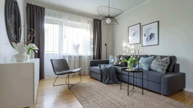 Ein modernes Wohnzimmer mit einem grauen Sofa, einem schwarzen Sessel, einer weißen Kommode und einem großen Spiegel.