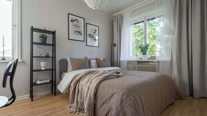 Ein Schlafzimmer mit einem Bett, einem Sessel, einem Regal mit Dekoration und einem Fenster mit Vorhängen.