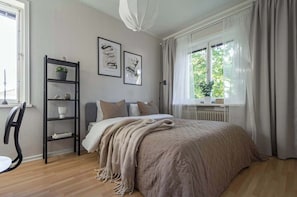 A bedroom with a bed, a chair, a shelf with decorative items, and a window with curtains.