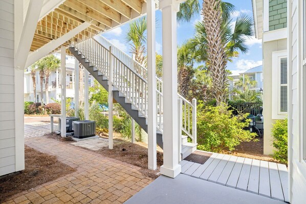 A covered outdoor area with a staircase leading to a deck, surrounded by palm trees and a brick pathway.