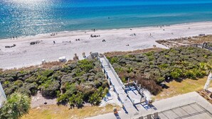 Une plage avec une promenade en bois qui mène à une zone sablonneuse, le tout entouré d’une végétation luxuriante.