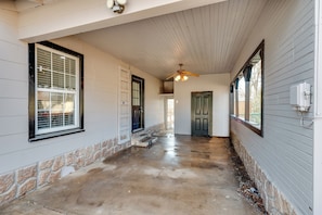 A covered porch with a concrete floor, a ceiling fan, and a stone baseboard.