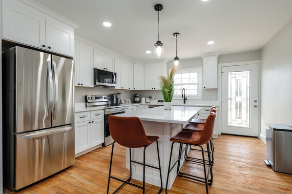 A modern kitchen with white cabinets, stainless steel appliances, a central island with stools, and pendant lighting.