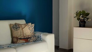 Un salon moderne avec un canapé blanc, un coussin décoratif, une petite plante posée sur un meuble blanc et un mur bleu.