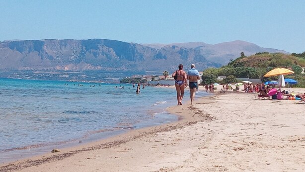 Une plage où l’on voit des gens se promener, des parasols et, en arrière-plan, des montagnes.