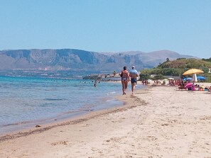 Ein Strand mit Menschen, Sonnenschirmen und einer Bergkulisse.