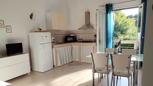Une cuisine compacte équipée d’un réfrigérateur, d’un four à micro-ondes et d’une cuisinière, un coin repas avec des chaises et une table, et un canapé dans l’espace salon.